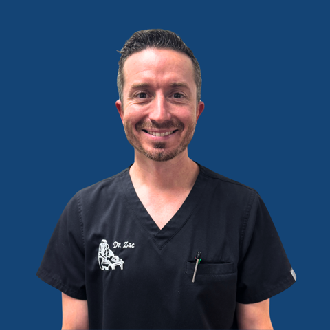 Chiropractor Fontana CA Zachary Cadman Meet The Team Zachary Cadman smiling in black scrubs with name and the business logo on the left side of chest in front of a blue background